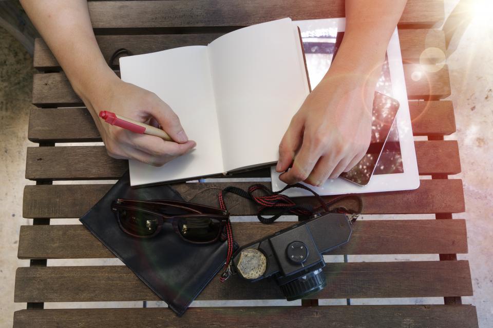 Two hands paging through an open notebook on a wooden table