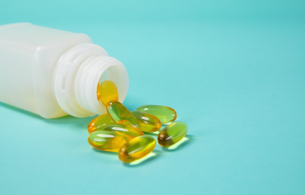 A white supplement bottle on its side with golden omega-3 capsules spilling out