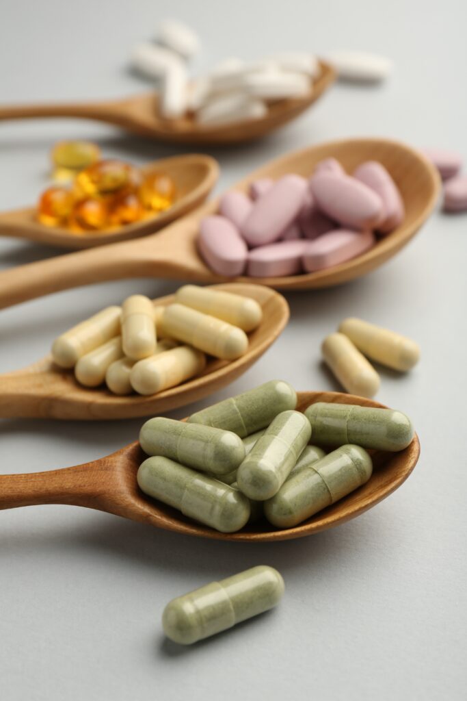 Wooden spoons holding green, cream, pink and amber supplement capsules and tablets