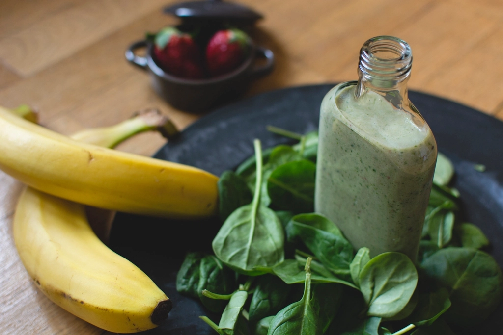 A green smoothie beside its ingredients on a wooden table