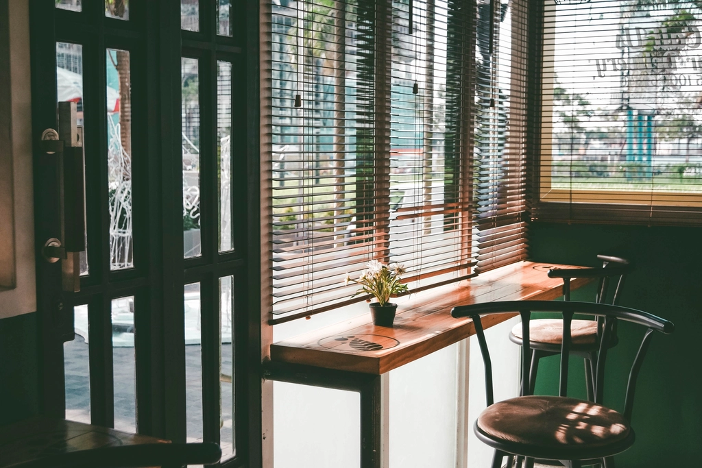 Stools at a wooden counter beside a window with the blinds half open