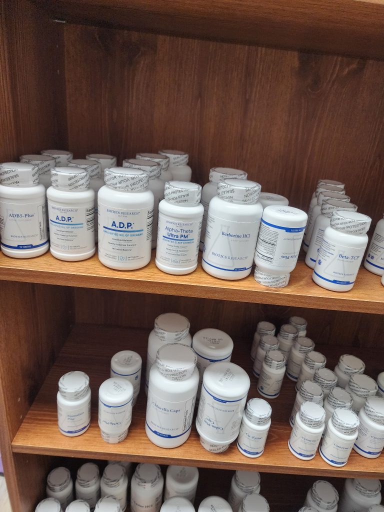 White bottles of practitioner-grade supplements lined up on a wooden shelf