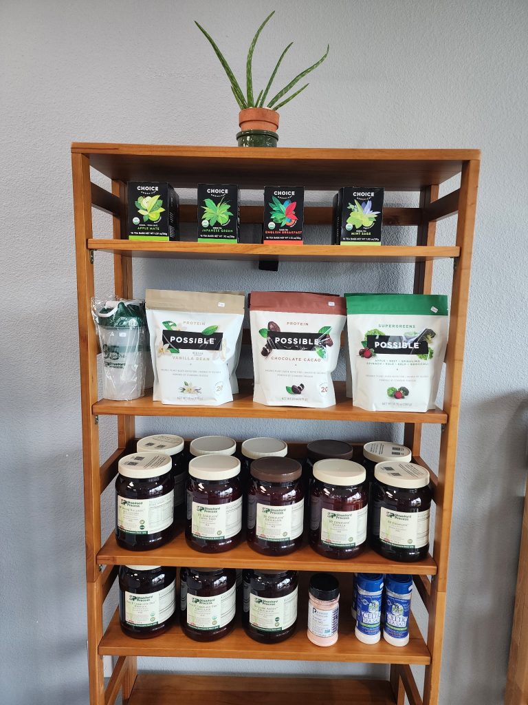 A wooden shelf in the store with organic snacks and jars of supplements, an aloe plant on top